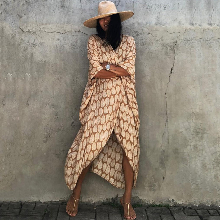 Frau in beige-gemustertem Kaftan und Strohhut vor Betonwand, Sommermode, lässiger Stil.