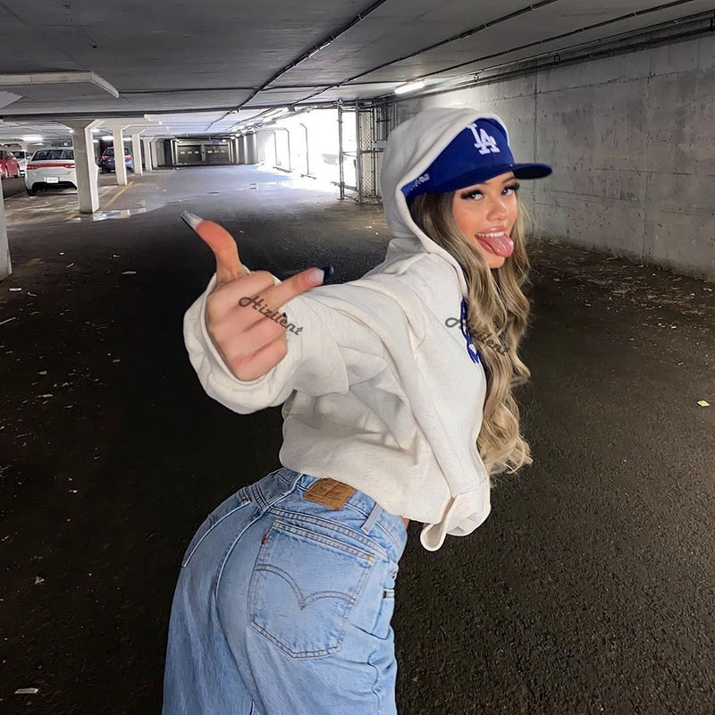 Frau in weißem Hoodie und blauer Kappe posiert in Tiefgarage, lässiger Streetwear-Look.