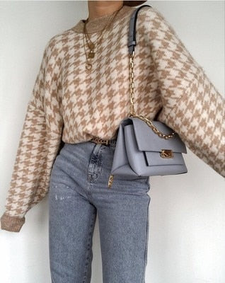 Frau in karierter Strickpullover, graue Jeans, graue Umhängetasche mit Kettengurt, modisch.