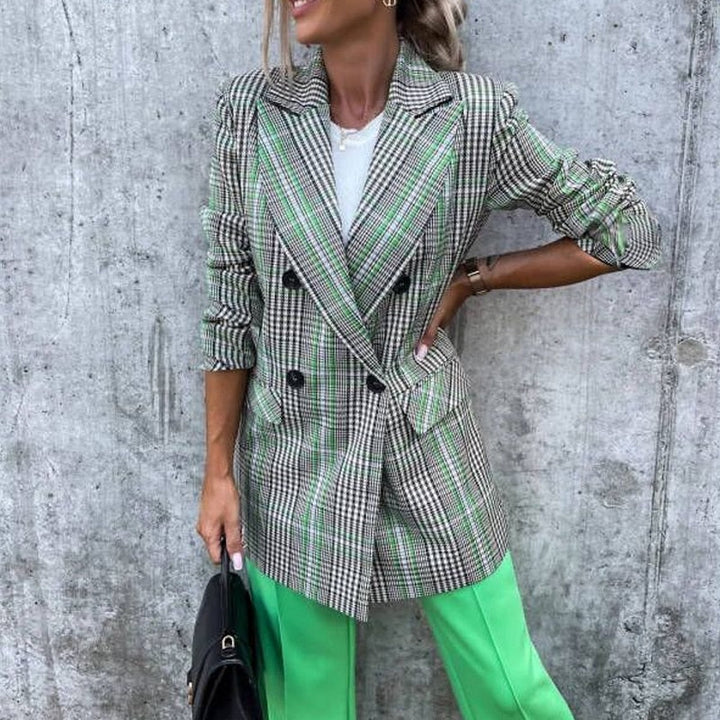 Frau in kariertem Blazer und grüner Hose vor Betonwand, modisch, elegant, Streetstyle.