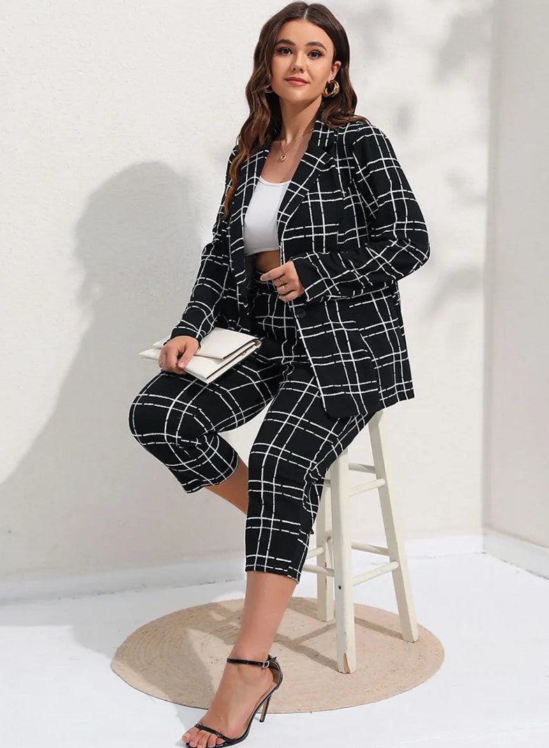 Frau in kariertem schwarzen Anzug, weißem Top, mit Clutch und Absatzsandalen, sitzt auf Hocker.