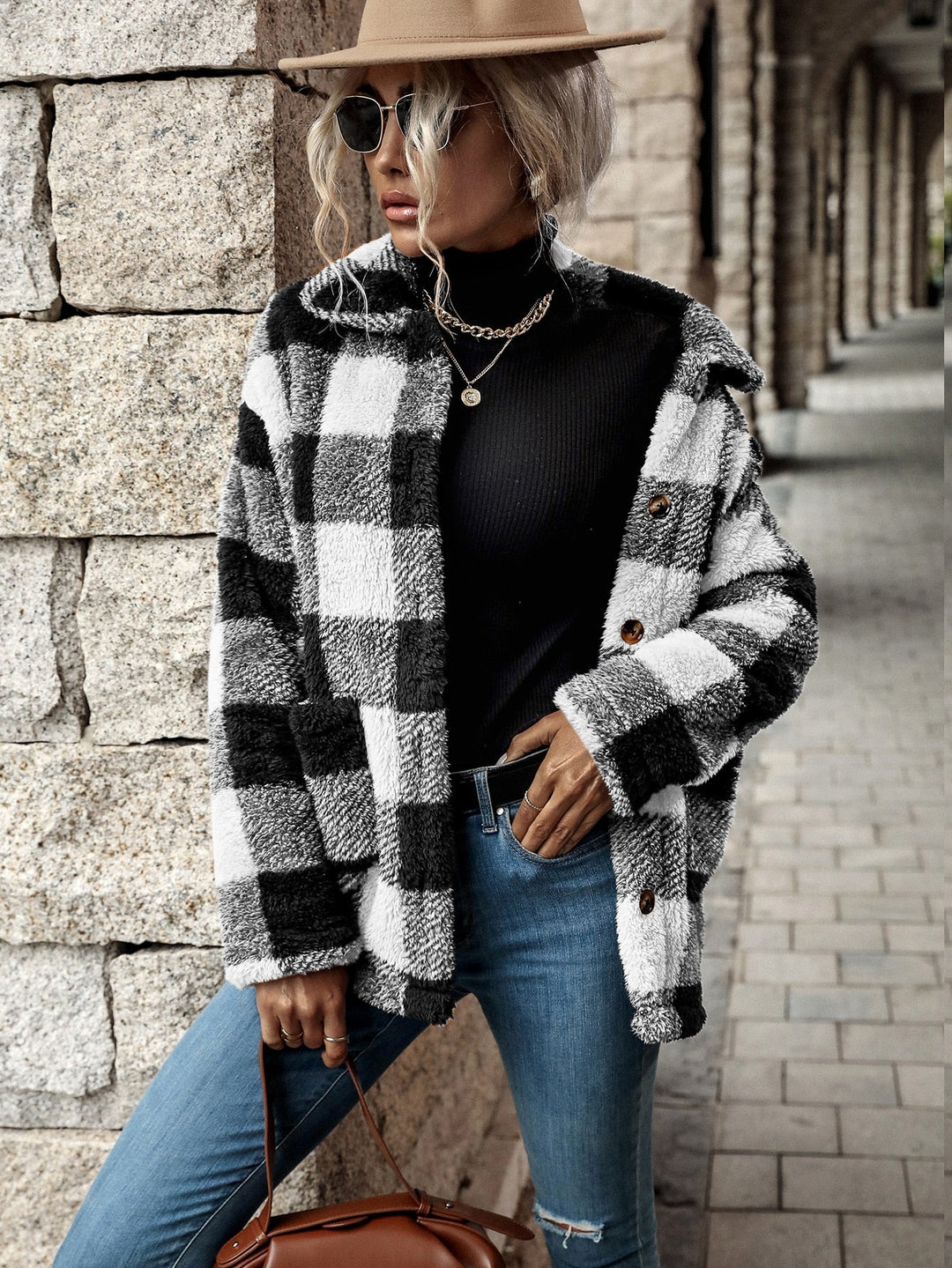 Frau in kariertem Wollmantel, schwarzem Rollkragenpullover, Jeans und Hut, modischer Herbstlook.