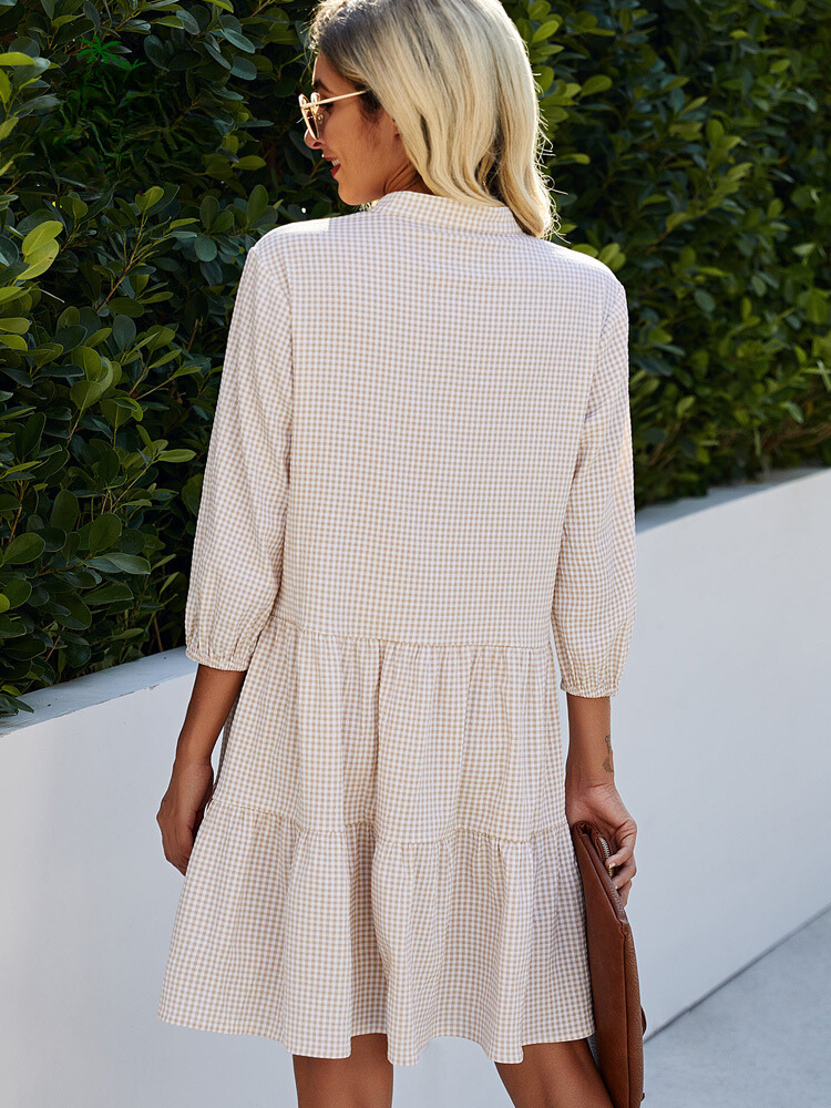 Frau in kariertem Sommerkleid, blond, Sonnenbrille, draußen, grüne Hecke im Hintergrund.