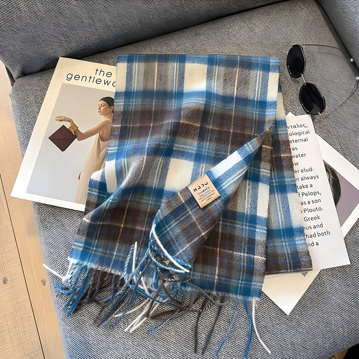 Blau-weiß karierter Wollschal mit Fransen auf grauem Sofa, modisches Accessoire.