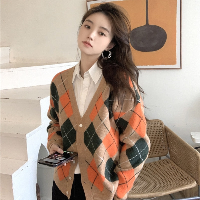 Frau in kariertem Strickjacke, beige-orange-grün, hält Smartphone, modisch, lässig, modern.
