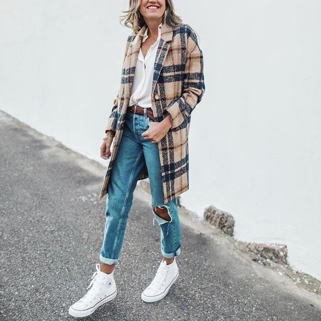 Frau in kariertem Mantel, blauer Jeans und weißen Sneakers auf Straße.
