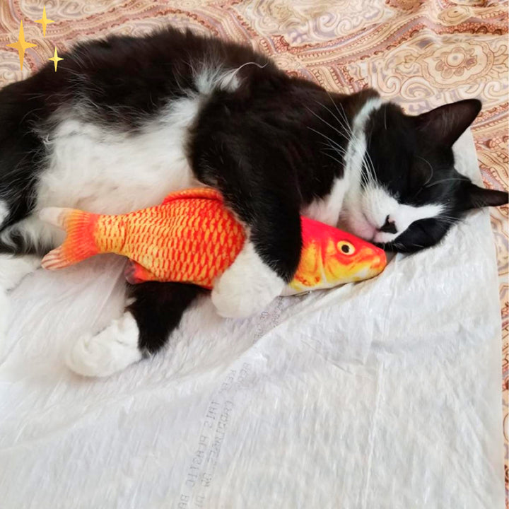 Schwarz-weiße Katze kuschelt mit orangefarbenem Plüschfisch auf gemustertem Bettbezug.