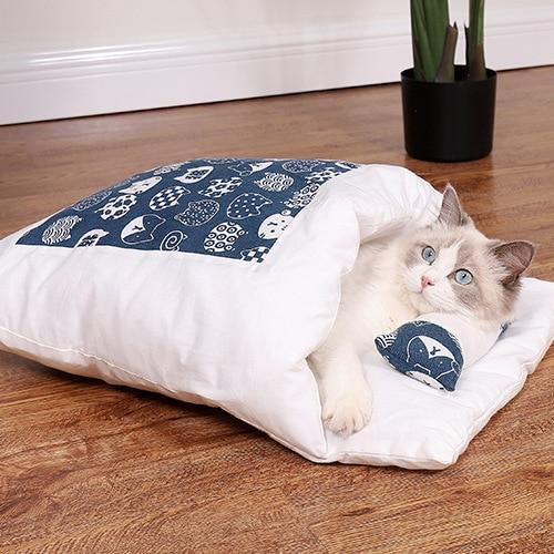 Katze in blau-weißem Schlafsack auf Holzboden, gemütlich, Haustierbett, Heimdekoration.