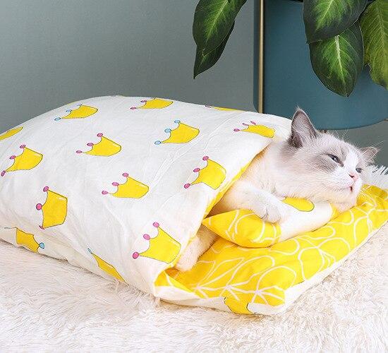 Katze in gelbem und weißem Kissenbett mit Kronenmuster, gemütlich auf Teppich liegend.