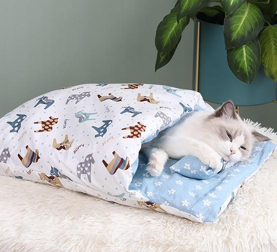 Schlafende Katze in bedrucktem Katzenbett mit Kissen, blau-weiß, gemütlich, Haustierbedarf.