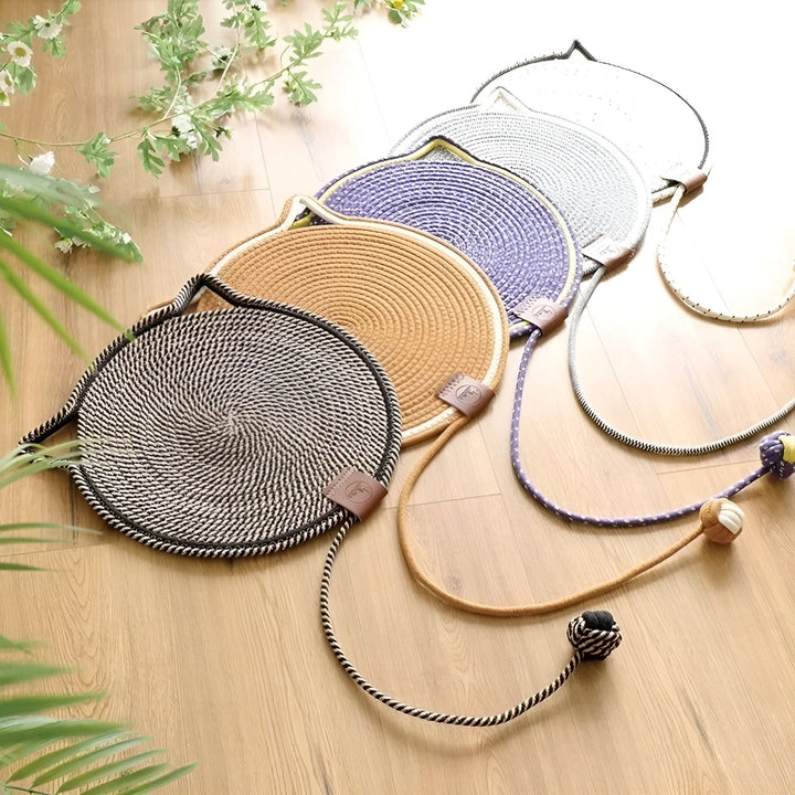 Geflochtene Katzenbettmatten in Schwarz, Beige, Lila und Grau auf Holzboden, mit Spielzeug.