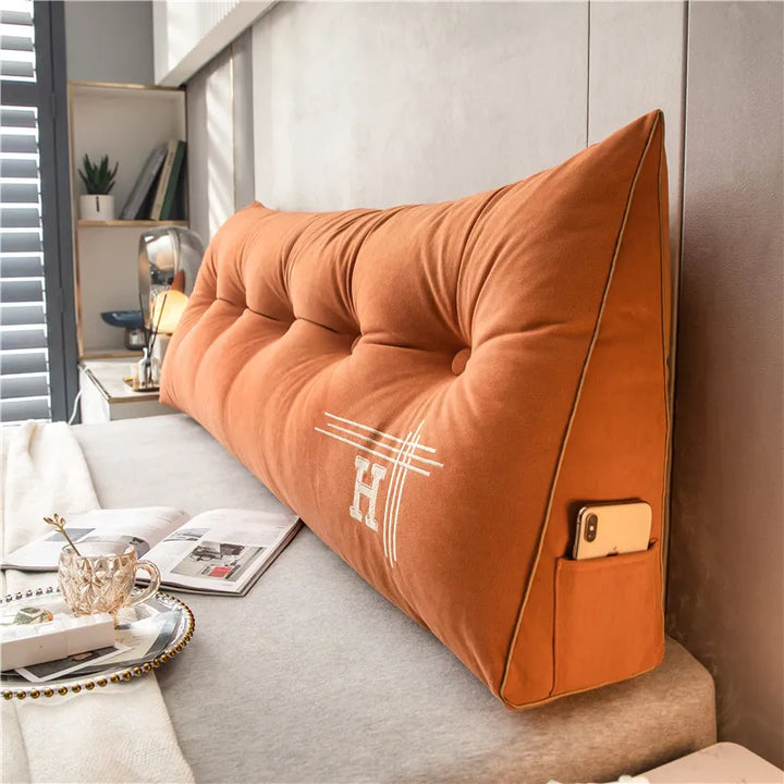 Orangefarbenes Keilkissen mit Taschen, gesticktem "H", ideal für Bett oder Sofa, modernes Design.