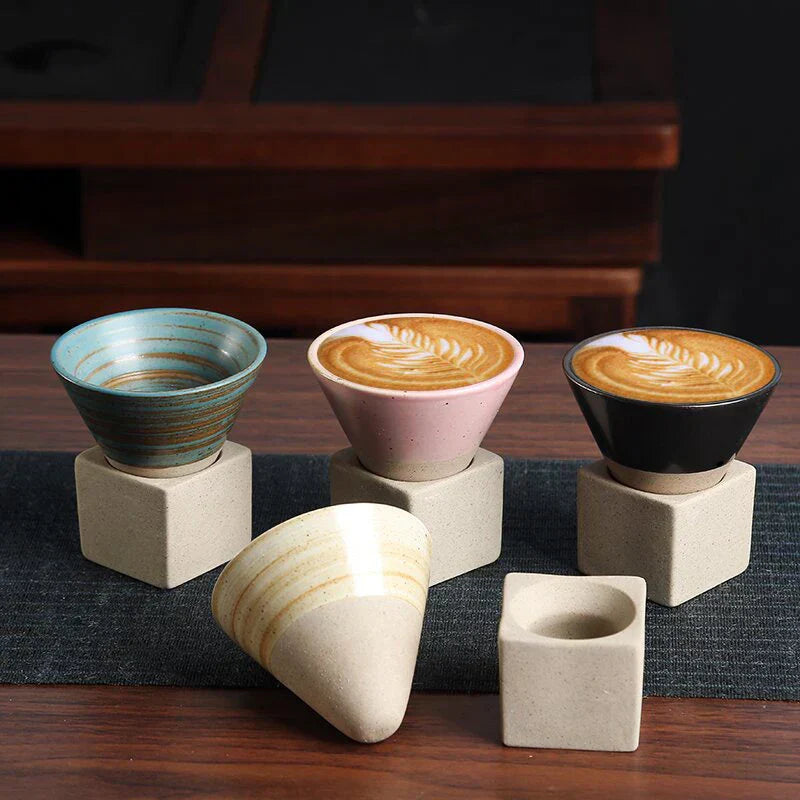 Drei bunte Keramik-Kaffeetassen auf Betonständern mit Latte Art, modern und stilvoll.