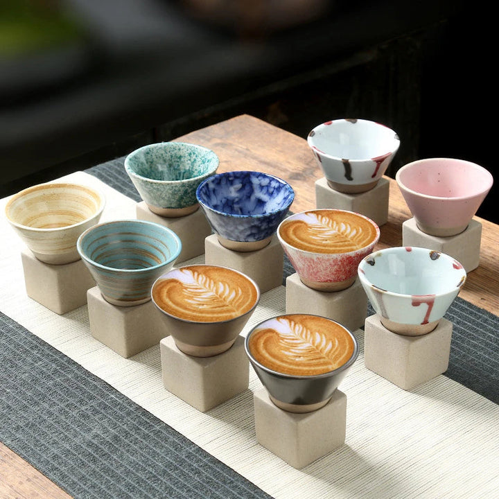 Neun bunte Keramikschalen auf Holzsockeln, handgefertigt, ideal für Kaffee oder Tee.