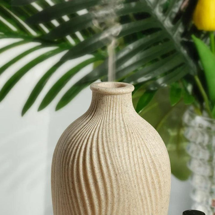 Keramikvase beige mit Rillenmuster, dekorativ, vor grünen Blättern, modernes Wohnaccessoire.