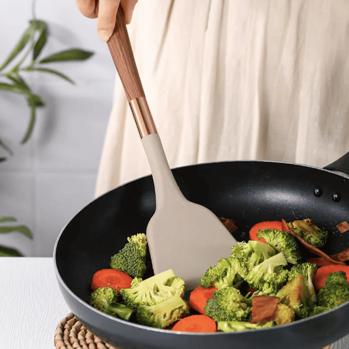 Moderne Silikon-Küchenutensilien mit Holzgriff, ideal zum Kochen von Gemüse in Pfanne.