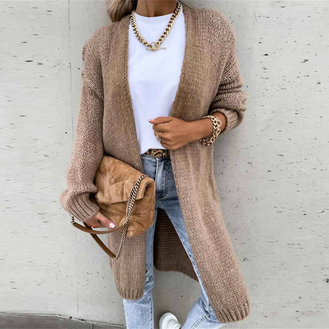 Frau in khakifarbenem Strickcardigan, weißem T-Shirt, Jeans, mit brauner Tasche und Goldkette.