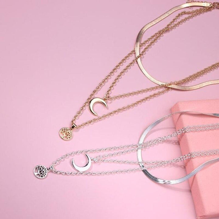 Goldene und silberne Halsketten mit Halbmond und Lebensbaum auf rosa Hintergrund.