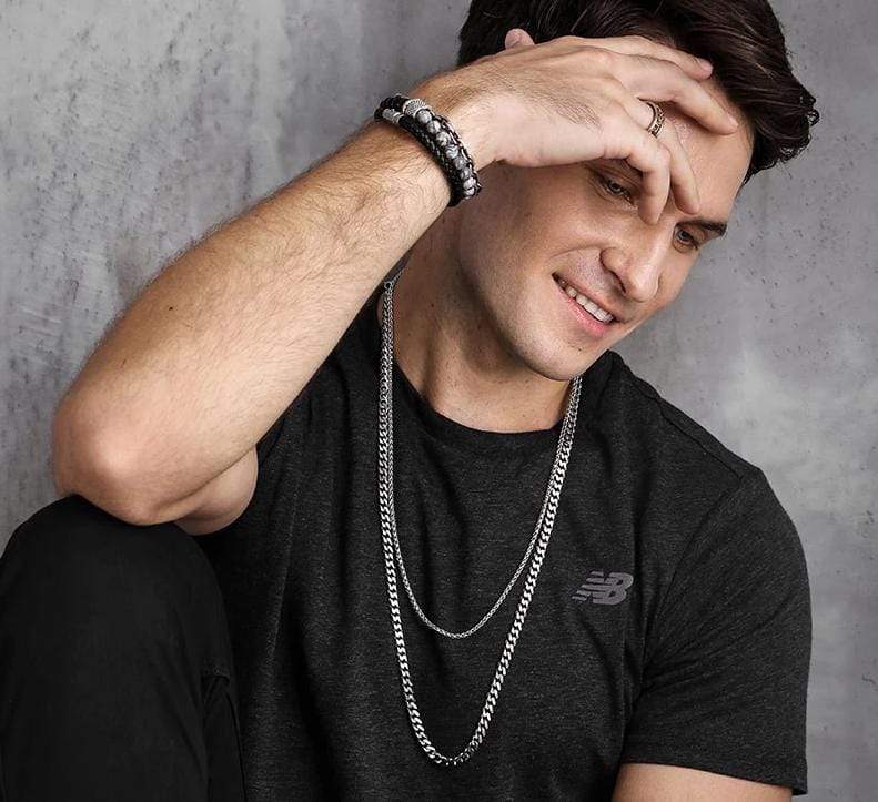 Mann mit Tigerauge-Perlenarmband, schwarzem T-Shirt, silberner Kette, lächelnd, lässiger Stil.