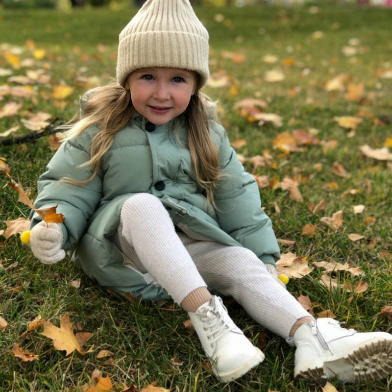 Mädchen in grüner Kinderparka, beige Mütze, Herbstlaub, Outdoor-Kleidung, warm, bequem.