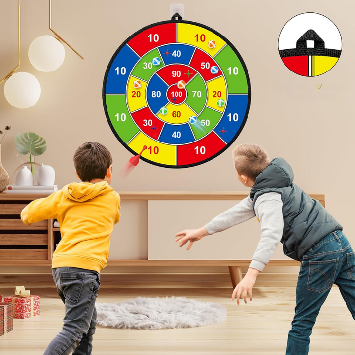 Zwei Kinder spielen mit buntem Klett-Dartspiel im Wohnzimmer, Zielscheibe an der Wand.