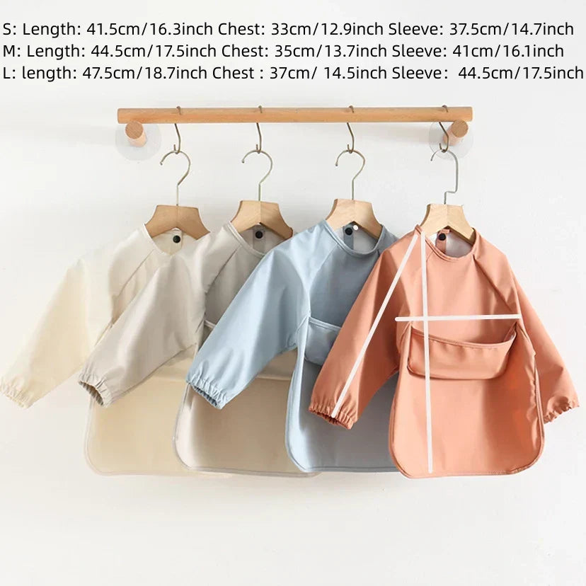 Vier Baby-Lätzchen mit Ärmeln, beige, blau, rosa, auf Holzkleiderbügeln, Größenangaben.