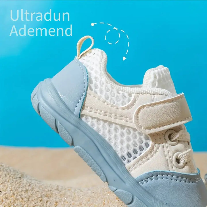 Beiger und blauer Kinderschuh, atmungsaktiv, mit Klettverschluss, auf Sandhintergrund.