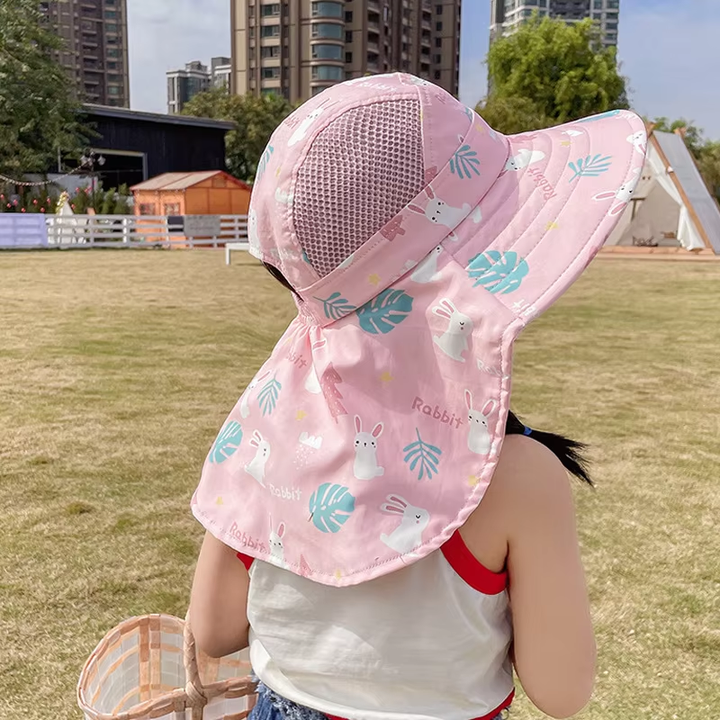 Mädchen mit rosa Sonnenhut mit Hasenmotiv im Park, Sonnenschutz, Kinderbekleidung.