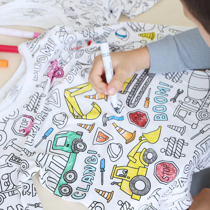 Kind malt auf T-Shirt mit Baufahrzeug-Motiven, Buntstifte, Kreativität, Kinderbekleidung.