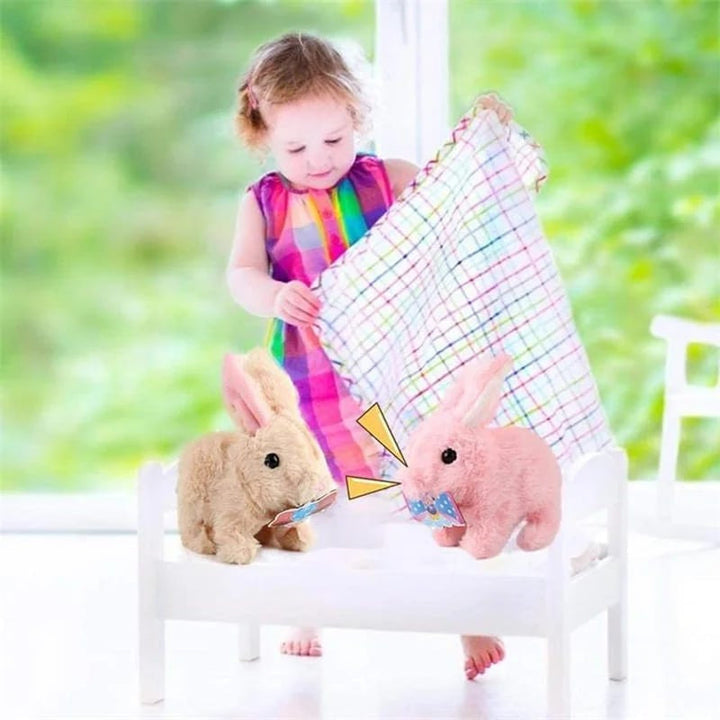 Kleinkind mit buntem Kleid spielt mit Plüschhasen auf weißem Bett, helles Zimmer.
