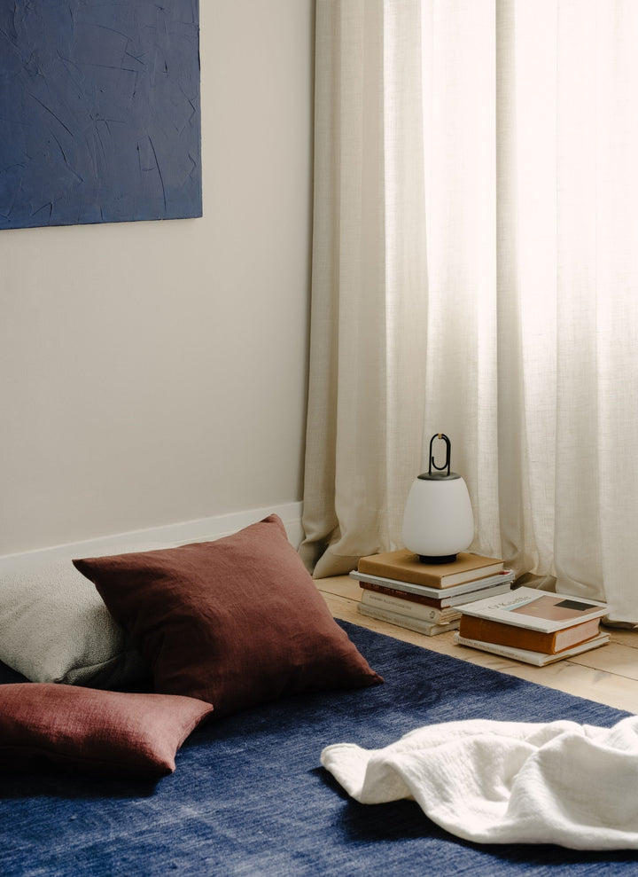 Gemütliches Wohnzimmer mit blauen Teppich, braunen Kissen, weißer Lampe und beigen Vorhängen.
