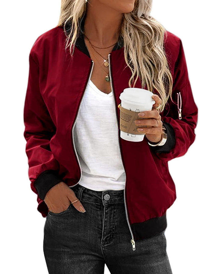 Frau in weinroter Bomberjacke, weißem T-Shirt, hält Kaffeebecher, lässiger Look.