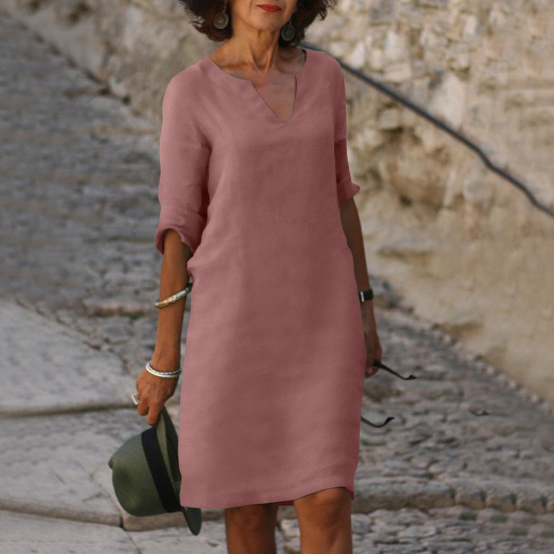 Frau in rosa Leinenkleid, V-Ausschnitt, knielang, auf Kopfsteinpflasterweg.