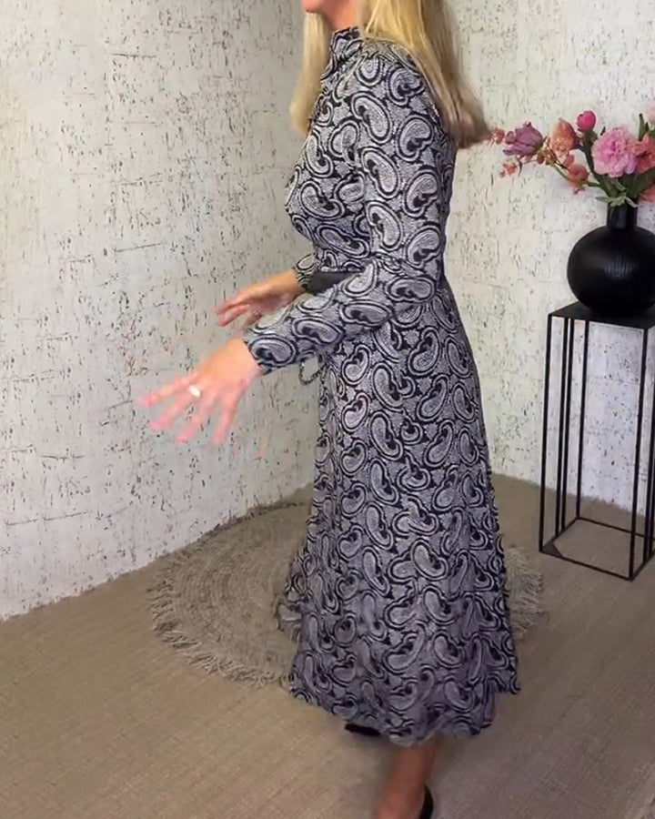 Frau in langem, gemustertem Kleid mit Paisley-Muster, Blumenarrangement im Hintergrund.
