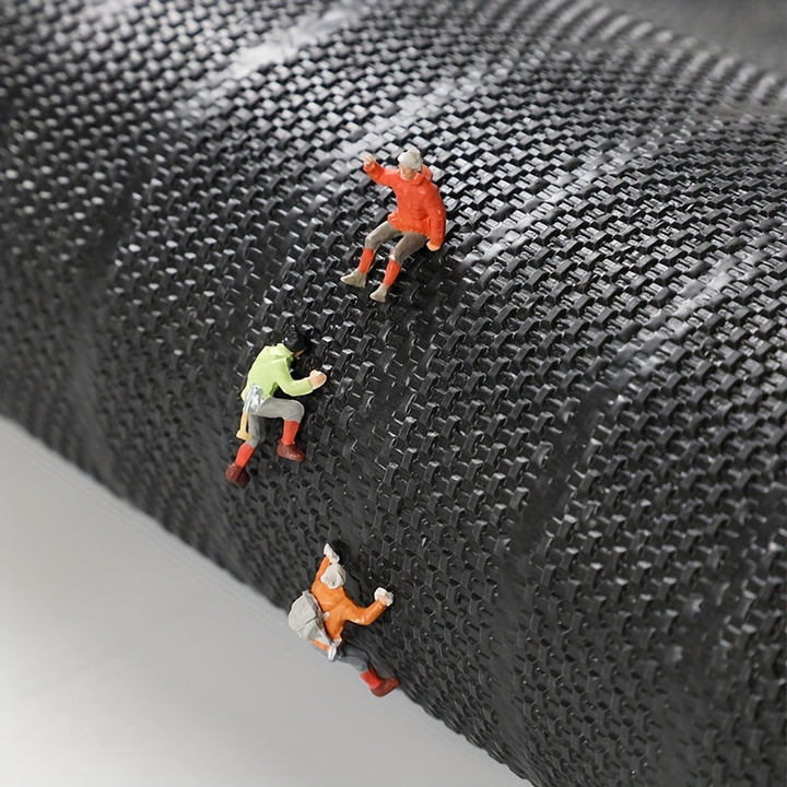 Miniatur-Bergsteiger auf schwarzem, strukturiertem Material, Klettern, Abenteuer, Detailaufnahme.