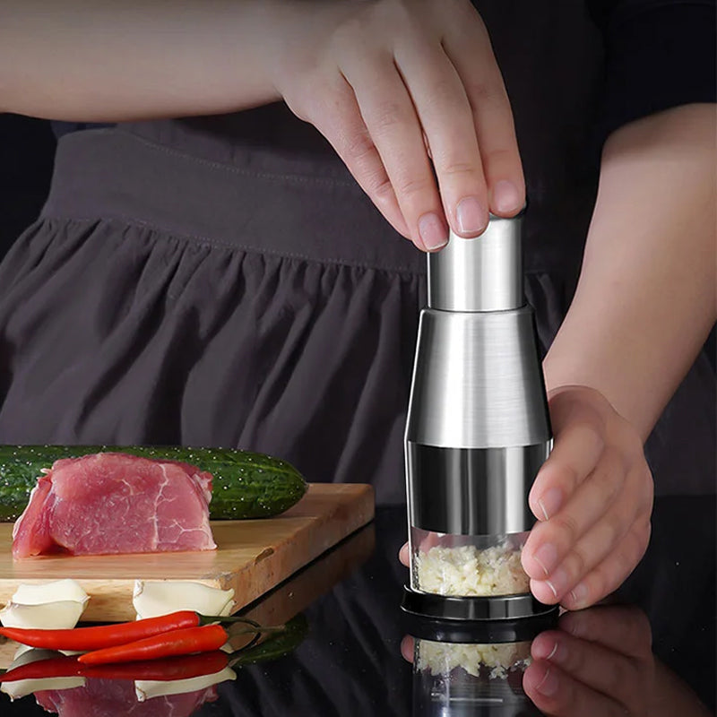 Person benutzt Edelstahl-Knoblauchpresse neben Schneidebrett mit Fleisch, Gurke und Chili.