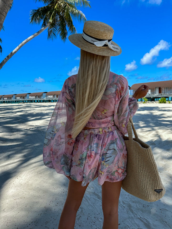 Frau im floralen Sommerkleid am Strand, Strohhut, Palmen, blauer Himmel, Urlaubsmode.