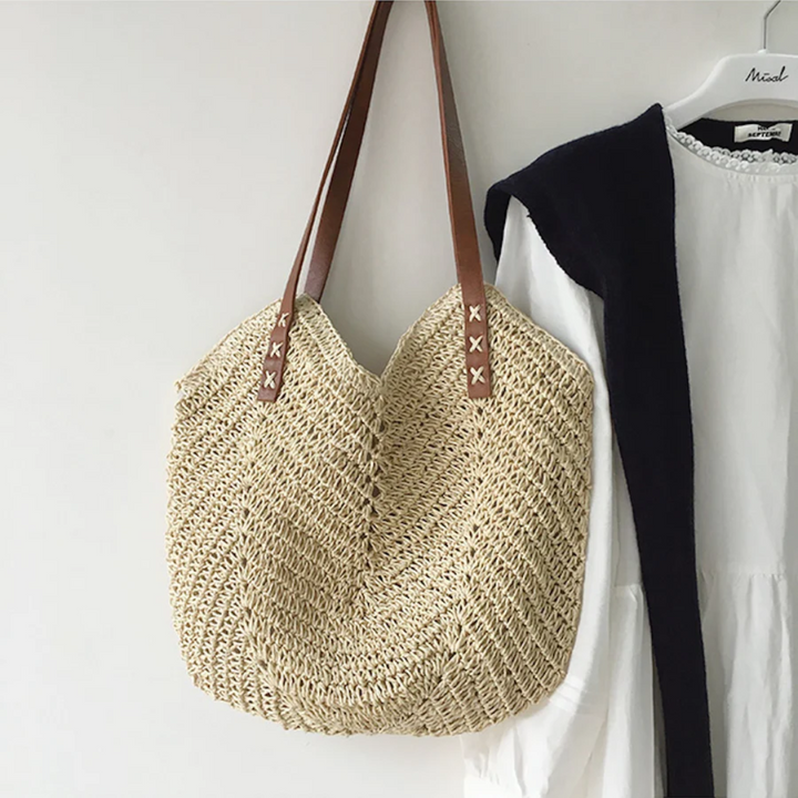 Strohtasche mit braunen Ledergriffen, handgefertigt, hängend an weißem Kleid, Boho-Stil.