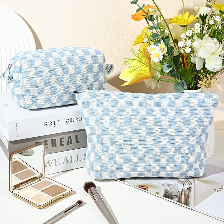 Hellblau-weiß karierte Kosmetiktasche aus Stoff, neben Blumenstrauß und Make-up-Pinsel.
