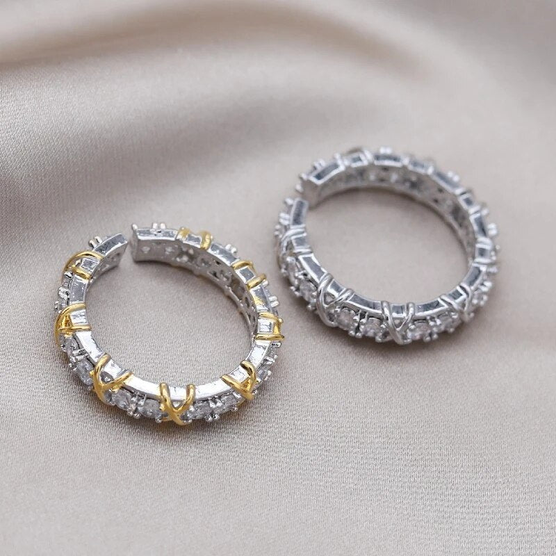 Zwei silberne Creolen mit Zirkonia-Steinen, eine mit goldenen Akzenten, auf beigem Stoff.