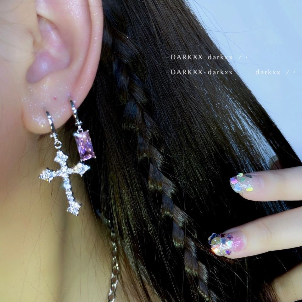Silberne Kreuz-Ohrringe mit rosa Stein, geflochtenes Haar, bunte Nageldesigns.
