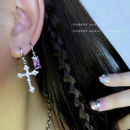 Silberne Kreuz-Ohrringe mit rosa Stein, geflochtenes Haar, bunte Nageldesigns.