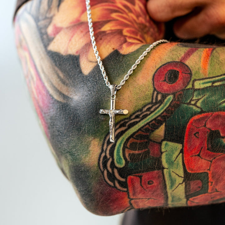 Silberne Kreuzkette auf tätowiertem Arm, Schmuck, Herrenaccessoire, modisch, Edelstahl.