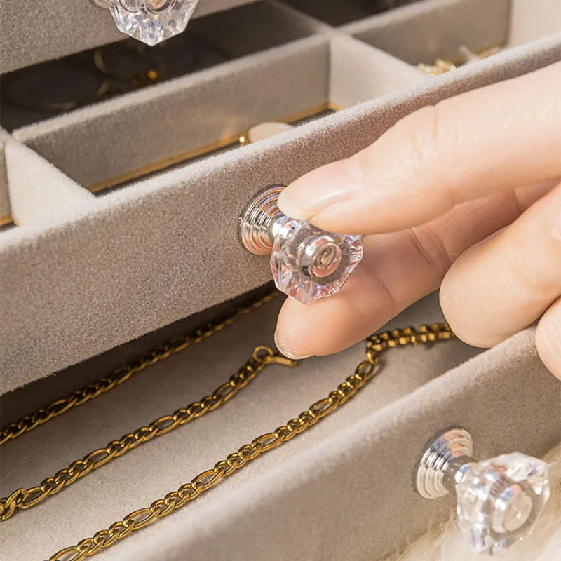 Hand greift nach Kristall-Schubladenknauf in Schmuckschatulle mit goldener Kette.