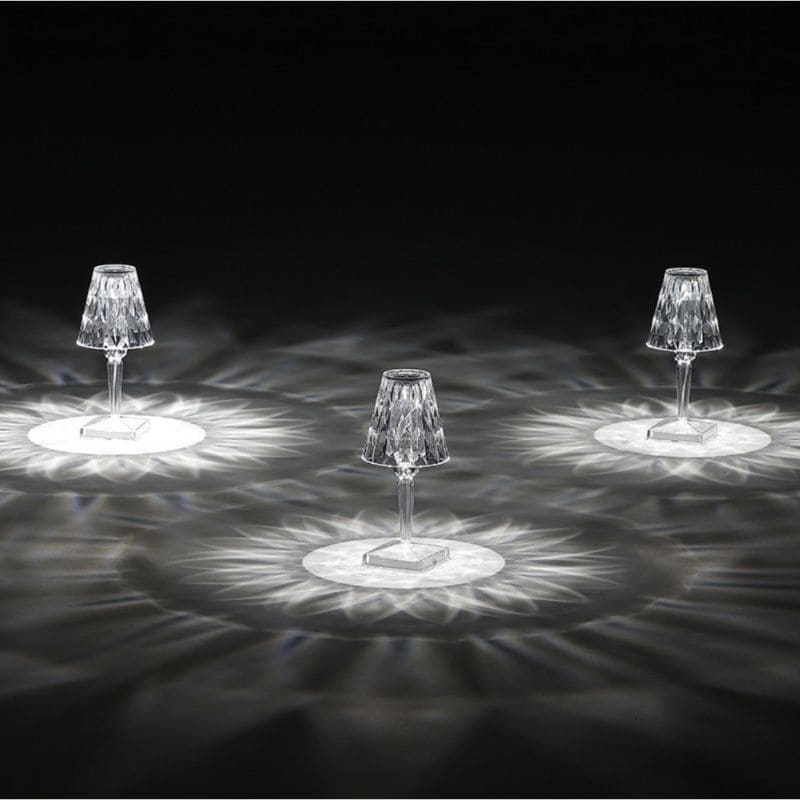 Drei kristallklare LED-Tischlampen mit facettiertem Schirm auf dunklem Hintergrund, elegantes Design.