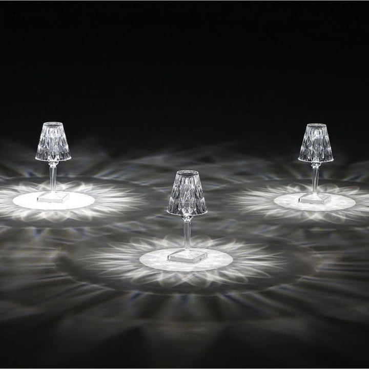 Drei kristallklare LED-Tischlampen mit facettiertem Schirm auf dunklem Hintergrund, elegantes Design.