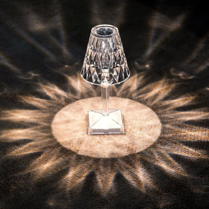 Kristall-Tischlampe mit facettiertem Schirm, strahlt dekoratives Lichtmuster auf dunklem Boden.