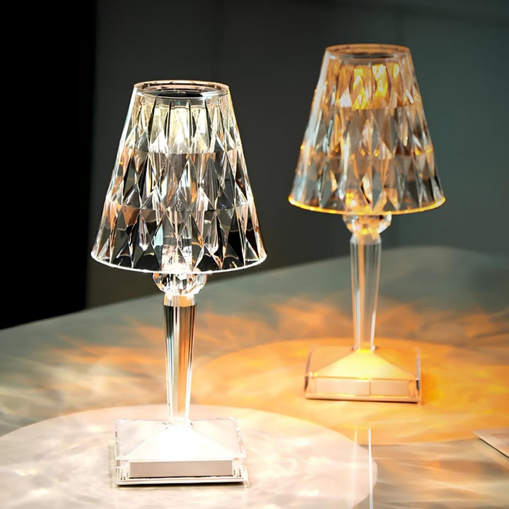 Kristall-Tischlampen, transparent, mit facettiertem Schirm, leuchtend auf weißem Tisch.