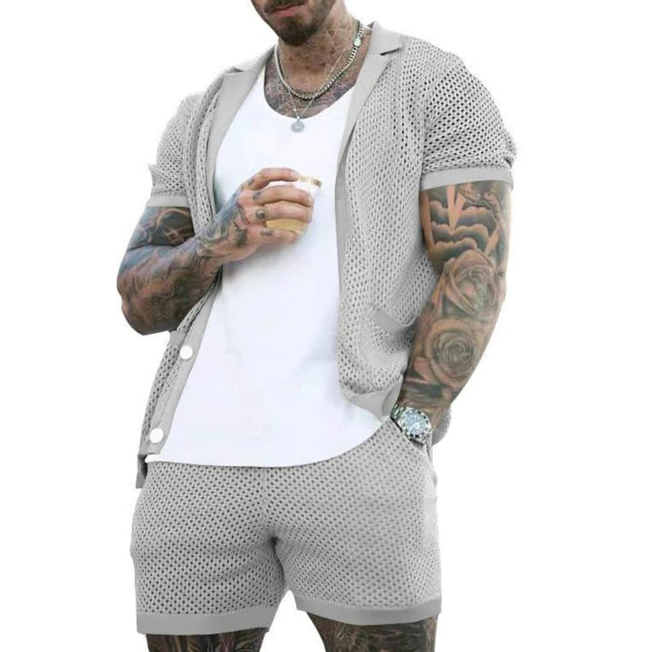 Mann in grauem Netz-Shorts-Set, weißes T-Shirt, tätowiert, hält Getränk, Sommermode.