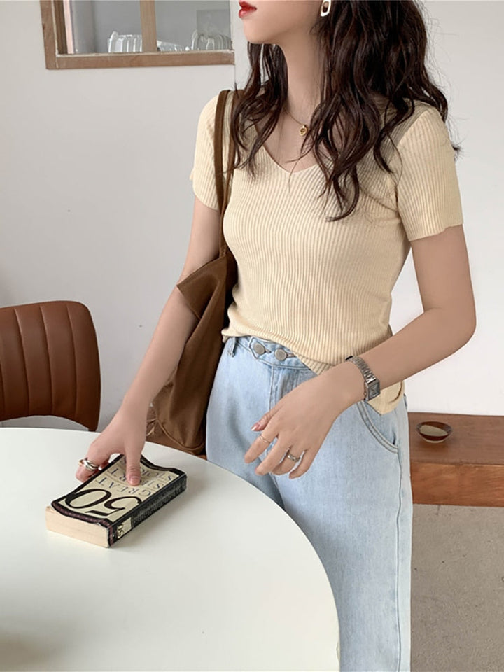 Frau in beigem Rippstrick-T-Shirt, hellblauer Jeans, brauner Tasche, hält Buch.